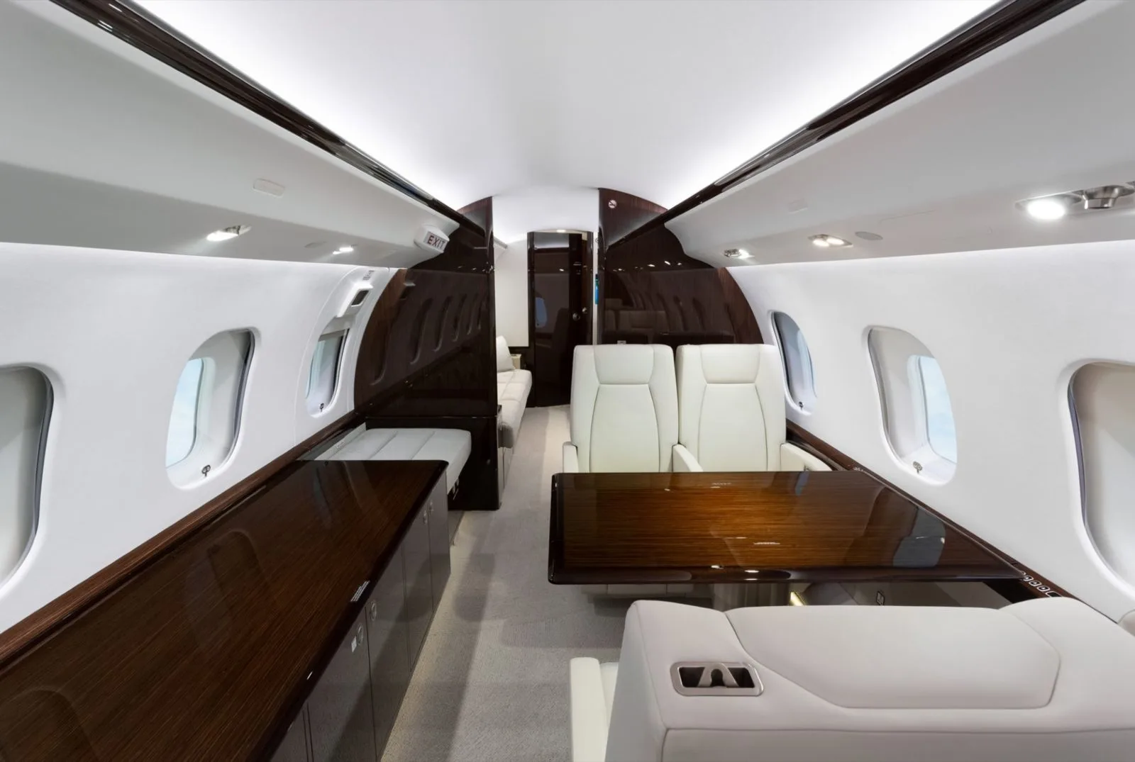 A luxurious aircraft cabin with white leather seats, dark wood accents, and a dining table.