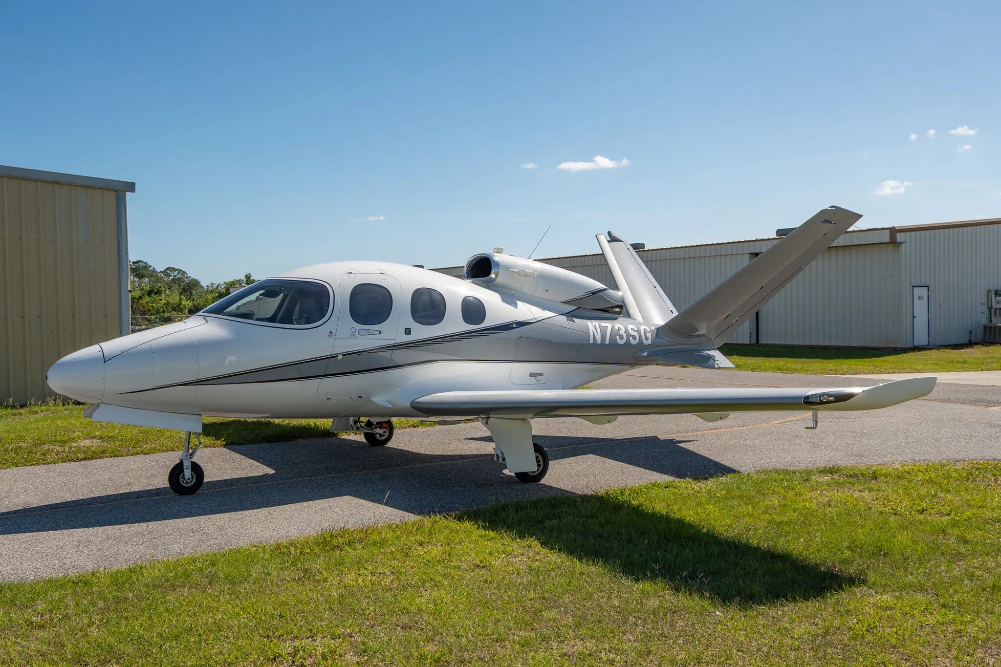 Front-side view of a white and grey Cirrus Vision Jet N73SG parked on an airfield.
