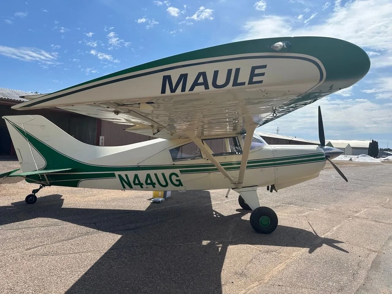 A Maule aircraft with a green and white paint scheme, showing 'MAULE' on the wing, is parked on an airfield.