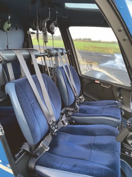 The blue upholstered cabin seats and harnesses inside a helicopter, viewed from the side.