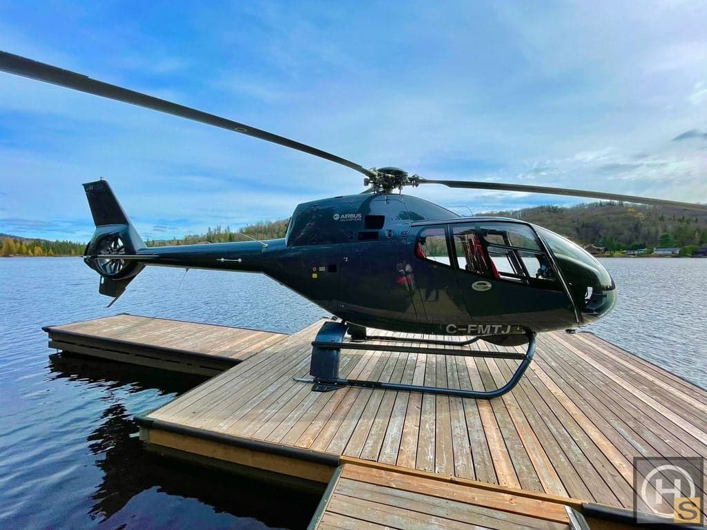 An Airbus helicopter, registration C-FMTJ, is parked on a wooden dock on a lake.