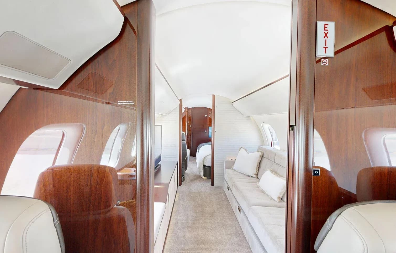A view down the private jet's luxurious cabin aisle, showcasing dark wood paneling and a light-colored sofa.