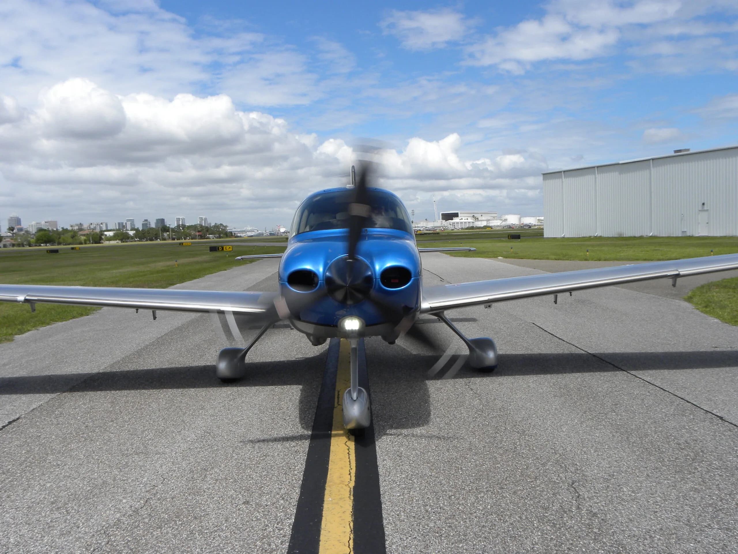 A head-on view of a blue and silver Cirrus SR22T aircraft, N313JB, with its propeller spinning on a taxiway.