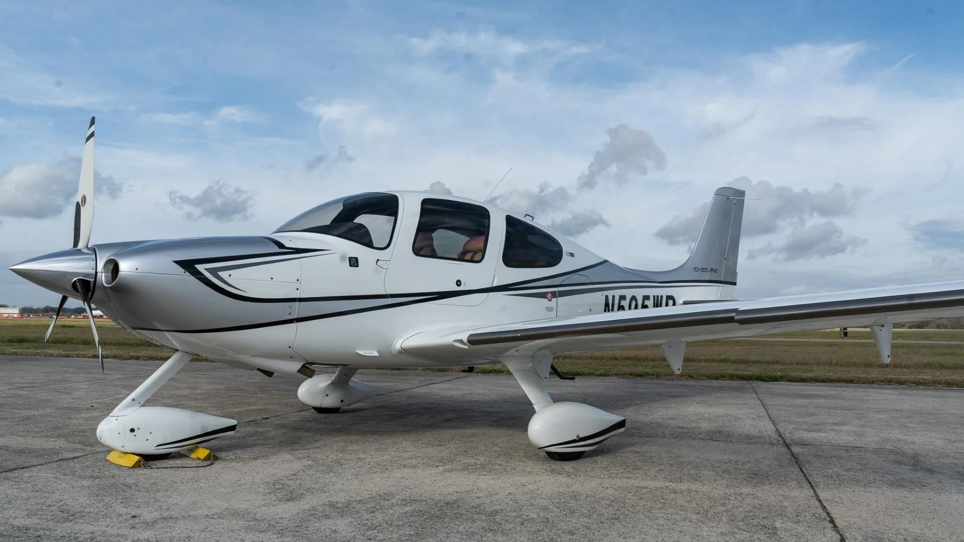 A white Cirrus SR22 aircraft with silver and black accents, registration N60EWD, parked on an airfield.