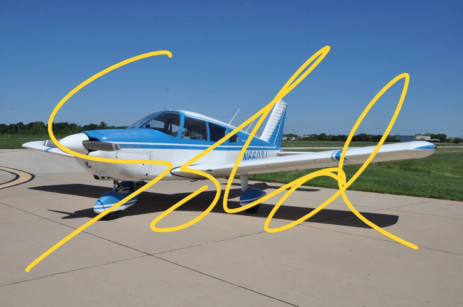 A white and blue Piper Cherokee D aircraft with registration N6600J is parked on an airfield under a clear blue sky, with a yellow 'SOLD' overlay.