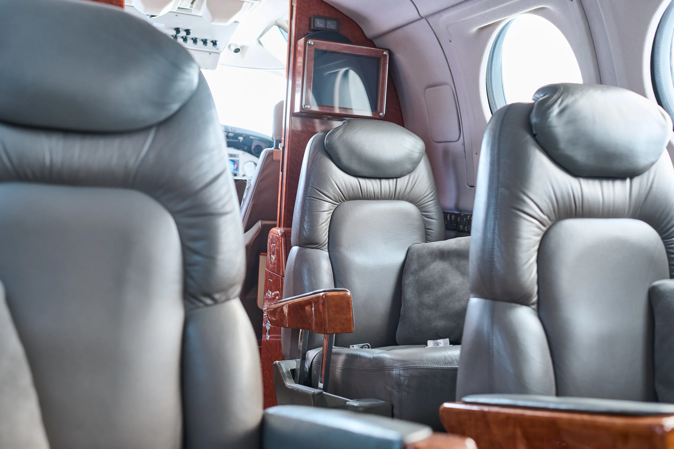 A close-up view inside the aircraft cabin shows grey leather seats and a small entertainment monitor.