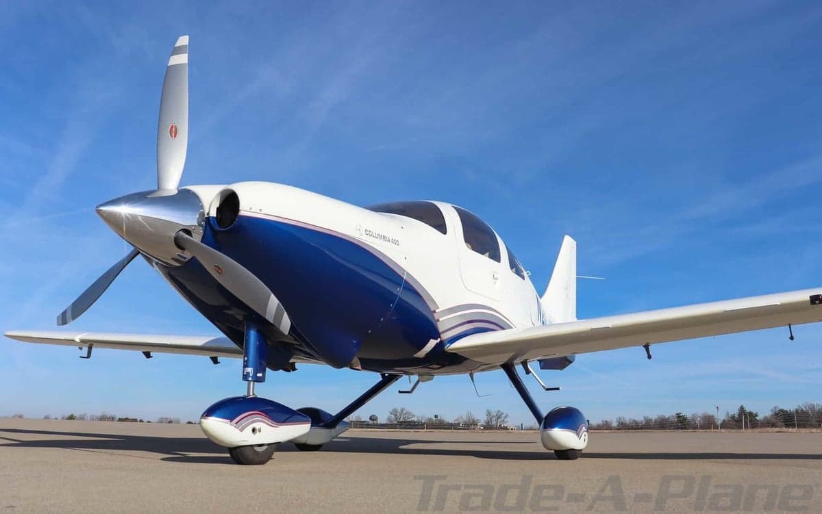 Low-angle front view of a white and blue Columbia 400 aircraft with a propeller on an airfield.
