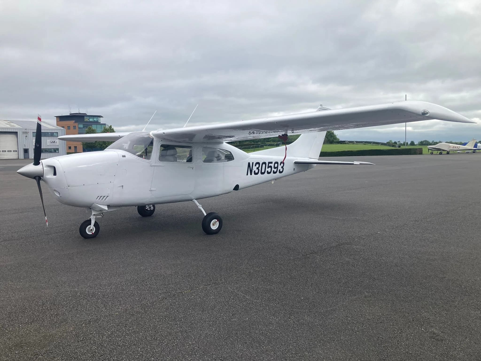 A white Cessna 172 aircraft N30593 parked on an airfield with buildings and another aircraft in the background.