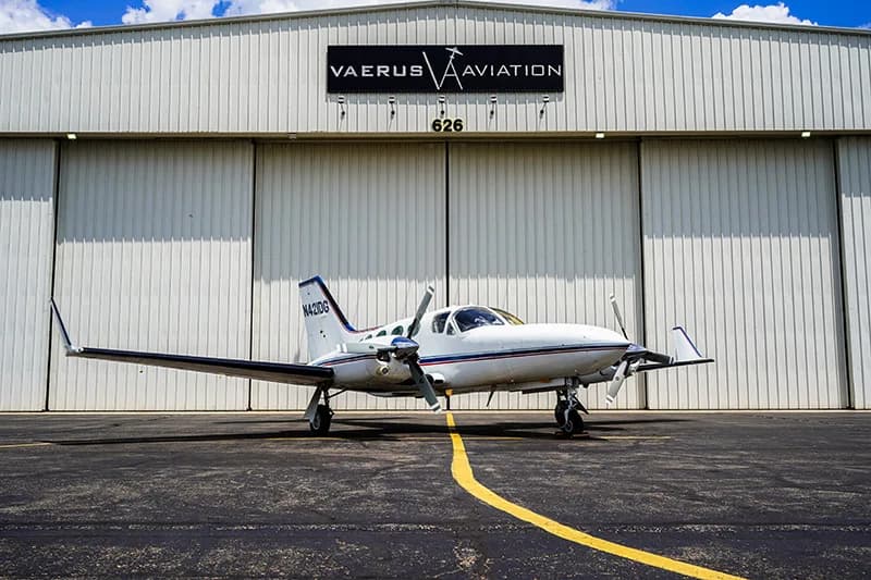 A Cessna 421 Golden Eagle aircraft is parked in front of a hangar with the Vaerus Aviation logo.