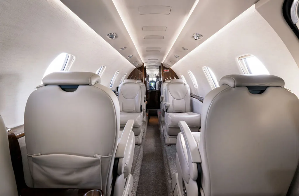 A view down the aircraft cabin aisle, showing rows of light-colored leather passenger seats.