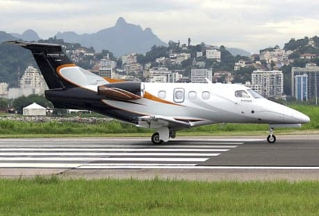 A Phenom 100 aircraft on the runway with a black, white, and orange paint scheme.