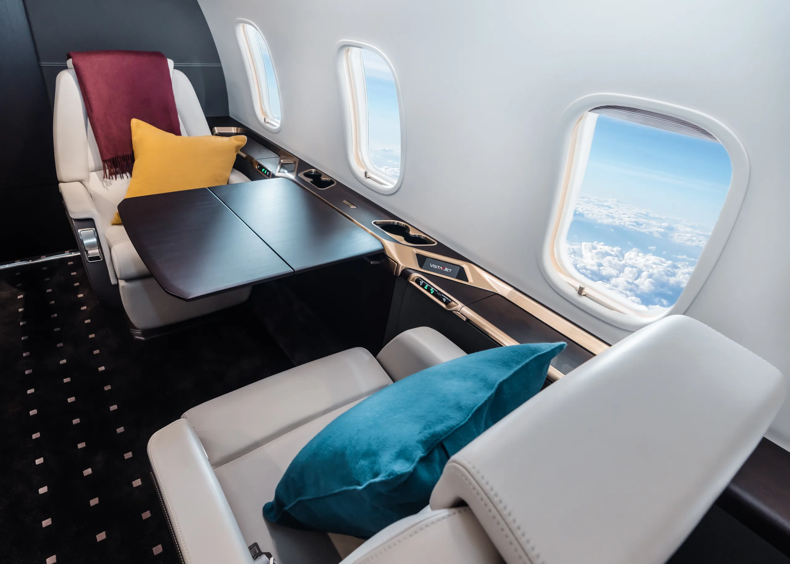 A jet interior with leather seats, a table, and a window view of clouds.