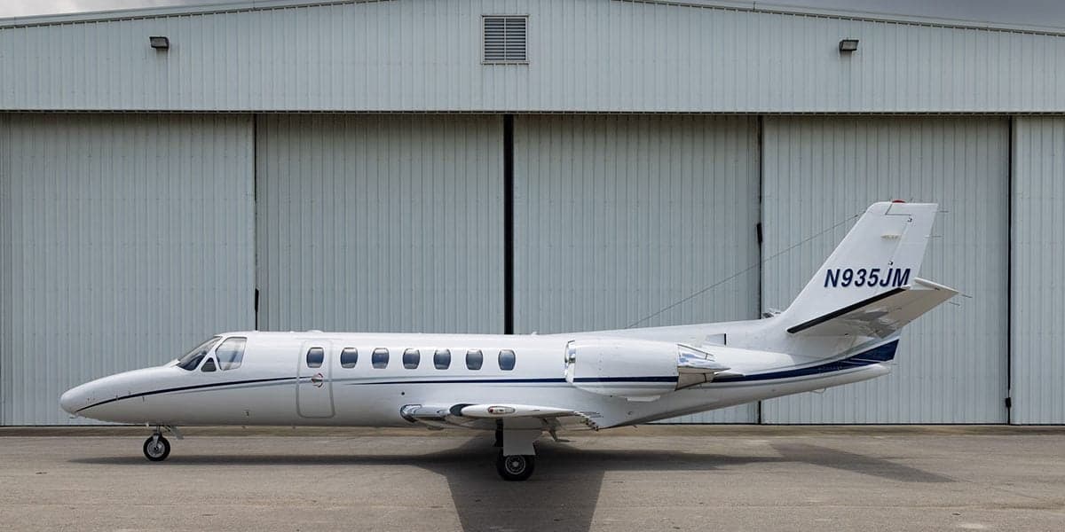 A Cessna Citation CJ3 aircraft is parked in front of a hangar, showing its side profile.