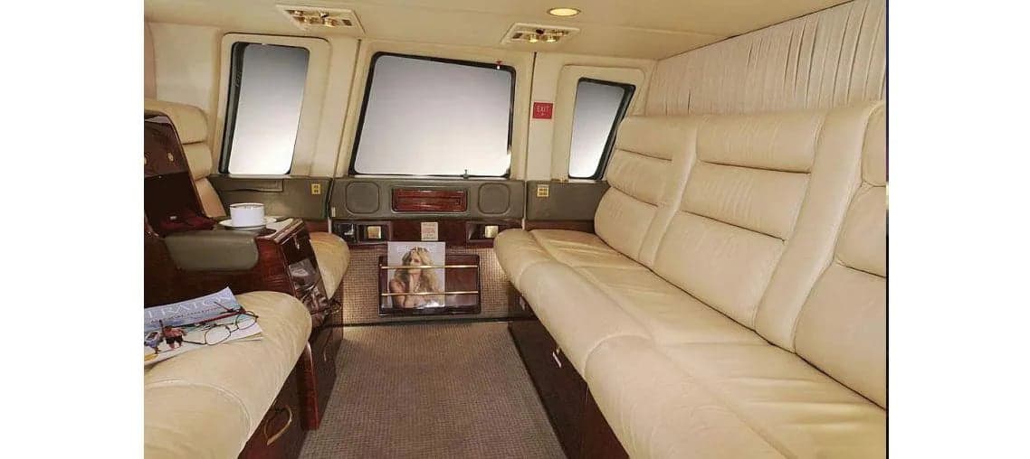 The helicopter's interior features cream-colored leather seats and wood trim.