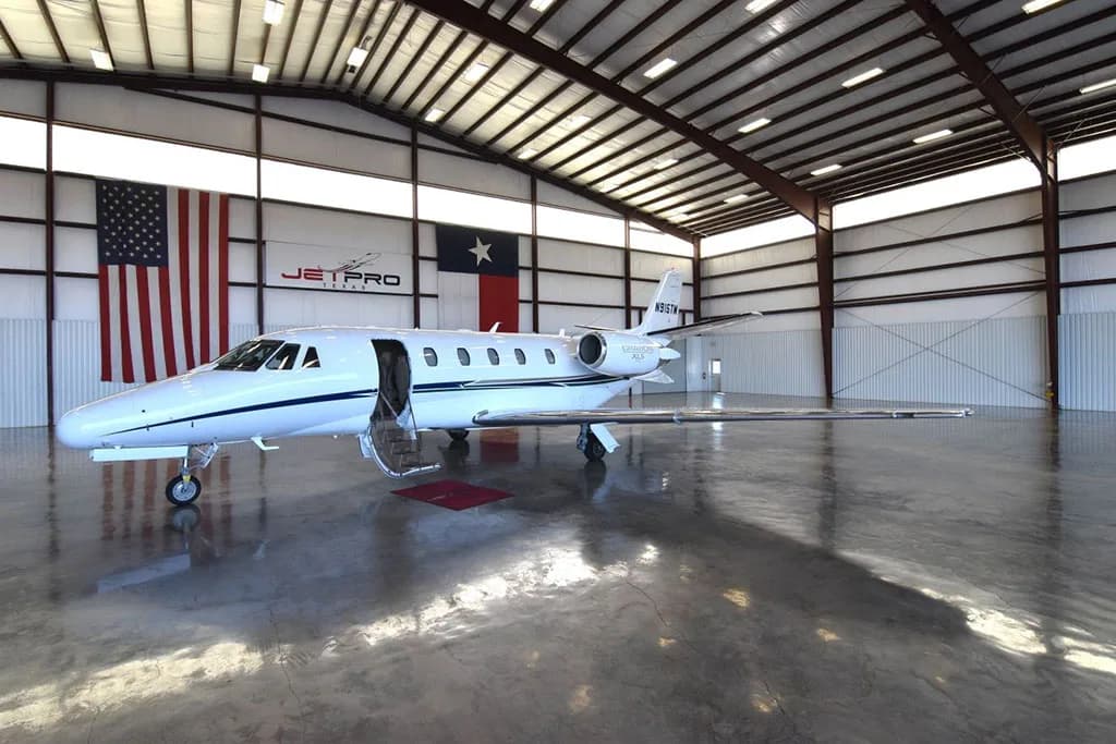 A white Cessna Citation XLS business jet with blue and silver stripes, tail number N915TM, parked in a hangar with its main cabin door open.