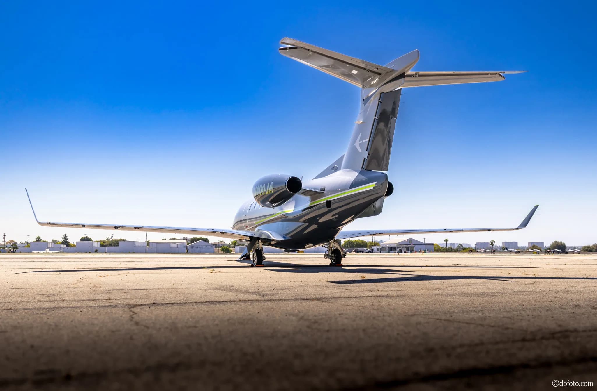 A grey Gulfstream business jet with green accents on its tail and engines, viewed from the rear on an tarmac under a clear blue sky.