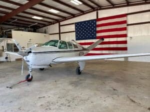A Beechcraft Bonanza aircraft parked in a hangar with an American flag in the background.