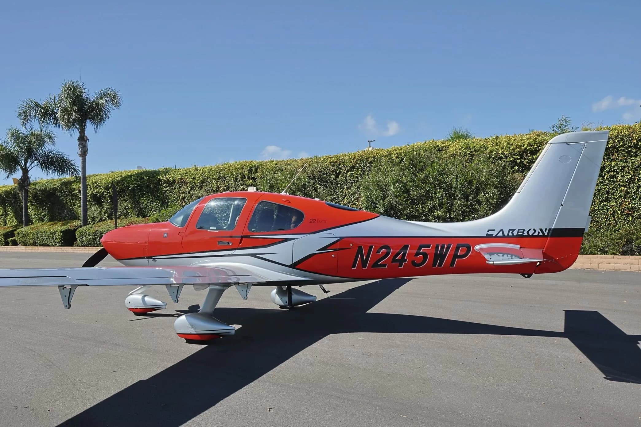 A red and silver Cirrus SR22 GTS aircraft, N245WP, parked on an tarmac with palm trees in the background.