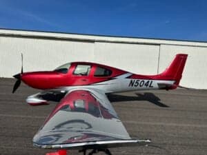 A Cirrus SR22T aircraft with a red and silver paint scheme is parked on a tarmac, showing the registration number N504L.