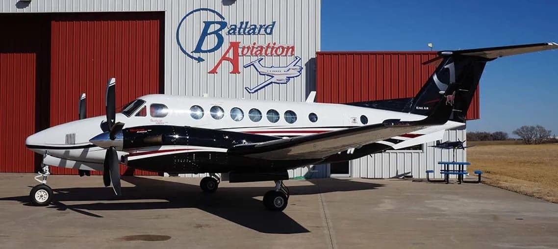 King Air turboprop aircraft with black and white paint scheme parked in front of a hangar.