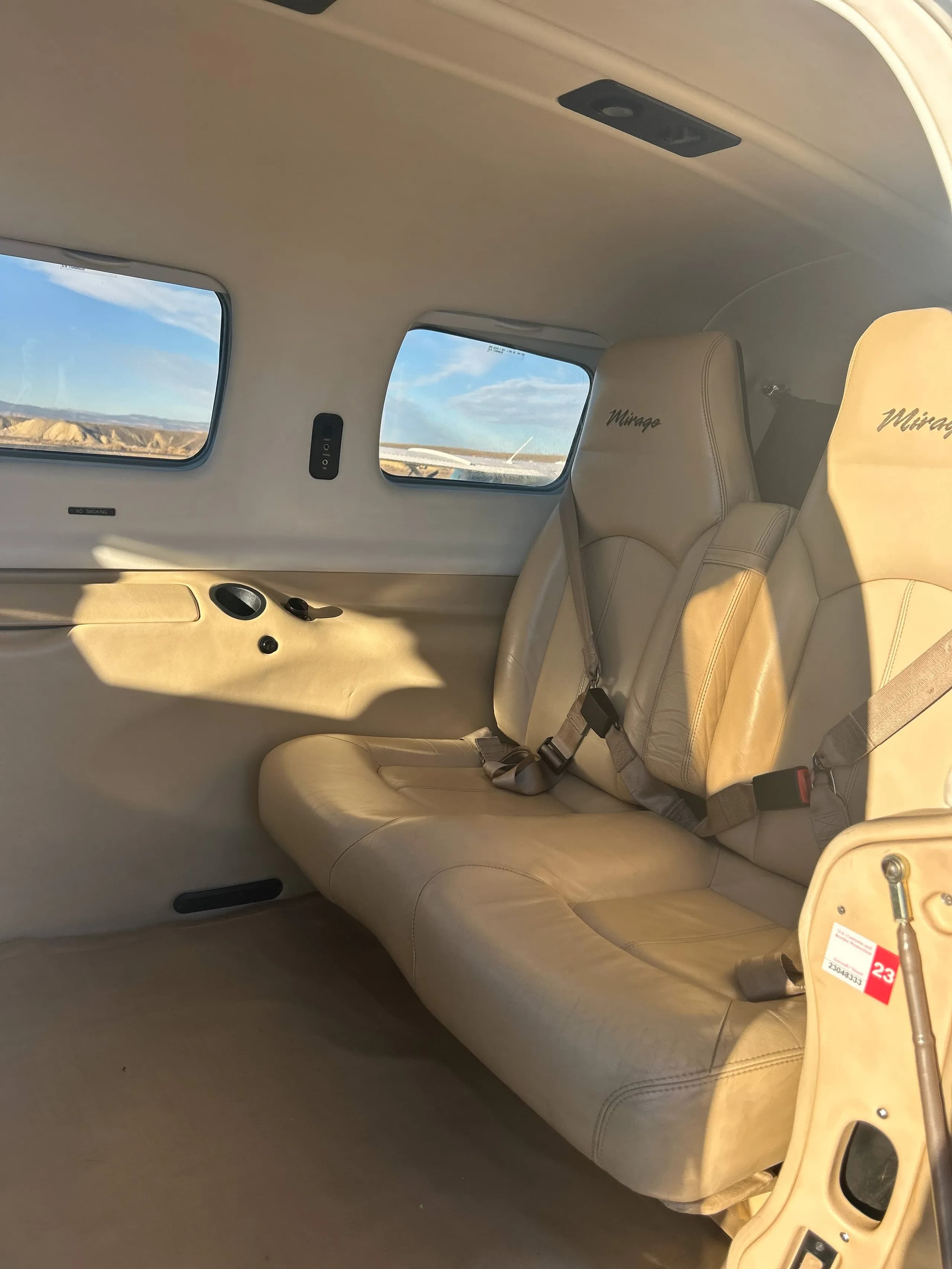 The beige leather interior cabin of the aircraft, showing two passenger seats and windows with a view of the outside.