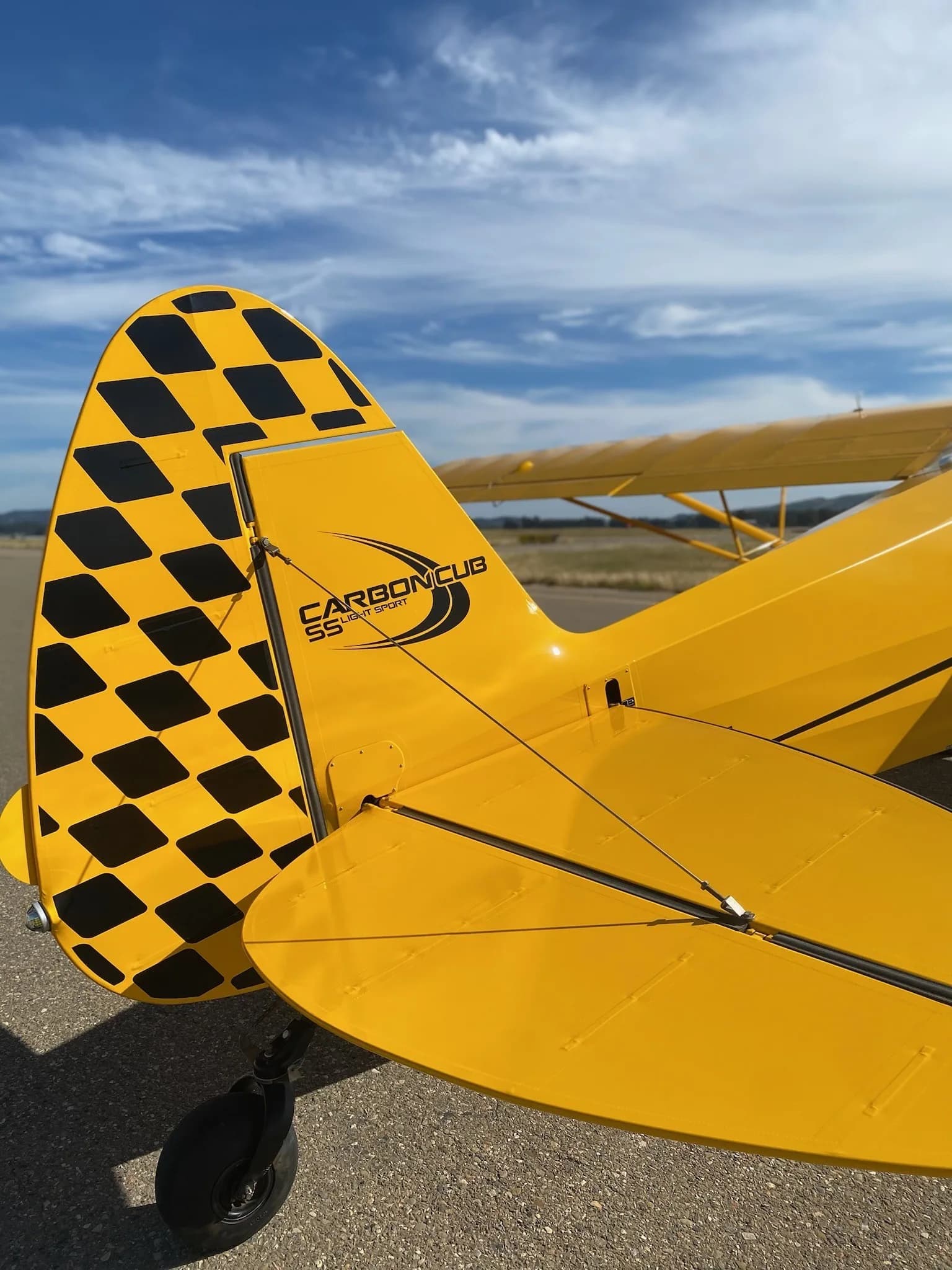 Close-up of the tail of a yellow Carbon Cub aircraft with a checkered pattern.