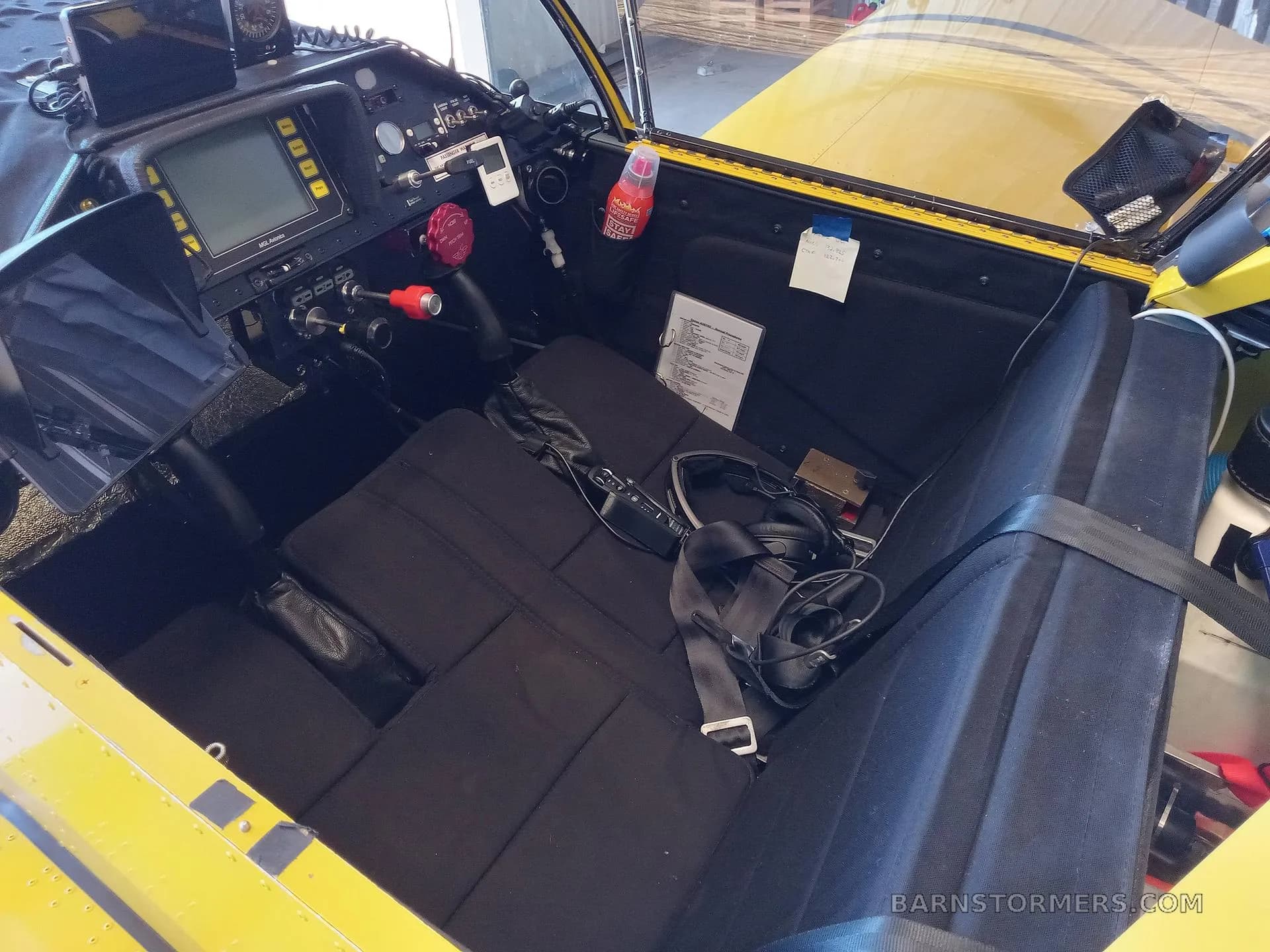 The interior of the yellow aircraft, showing the black seats, cockpit panel, and a headset on the seat.