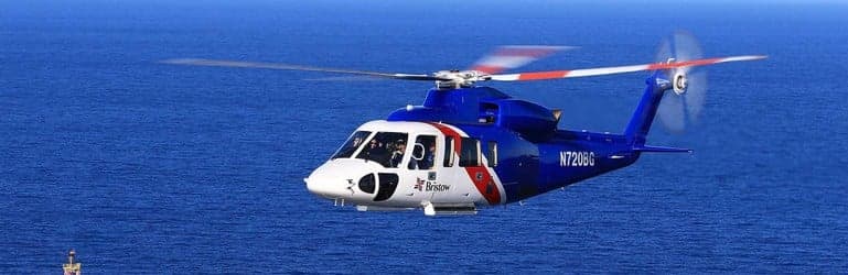 A blue and white Bristow helicopter flies over the ocean.