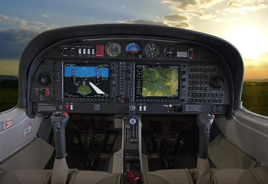 The cockpit of a Diamond aircraft with a modern glass panel display and a sunset sky visible through the windshield.