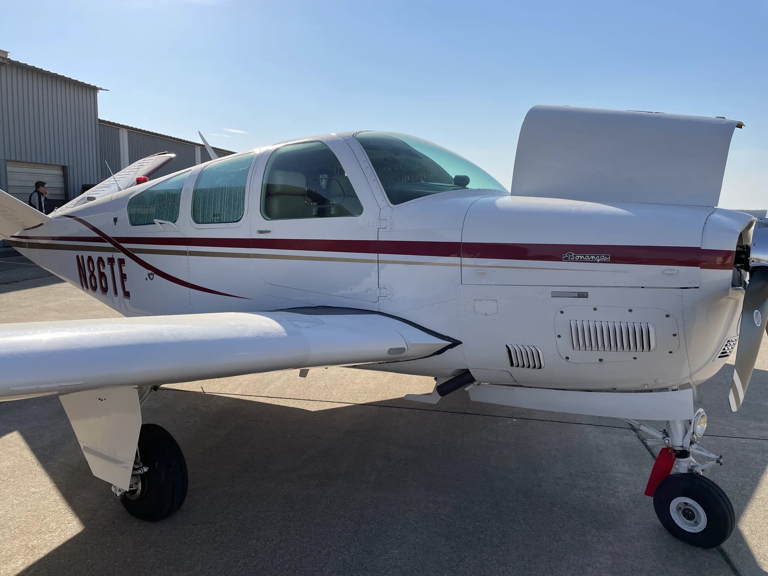 A white single-engine propeller aircraft, N86TE, with a red and gold stripe, parked on an airfield.