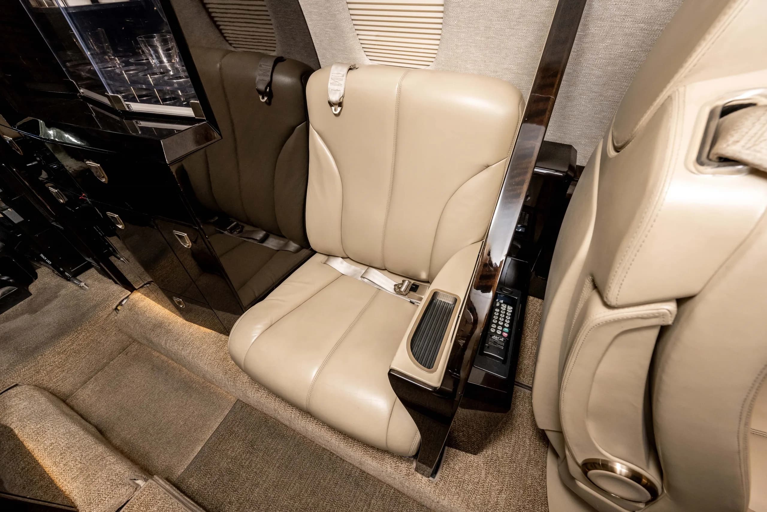 An overhead view of a light tan leather seat in a business jet cabin, showing the armrest controls and dark wood trim.