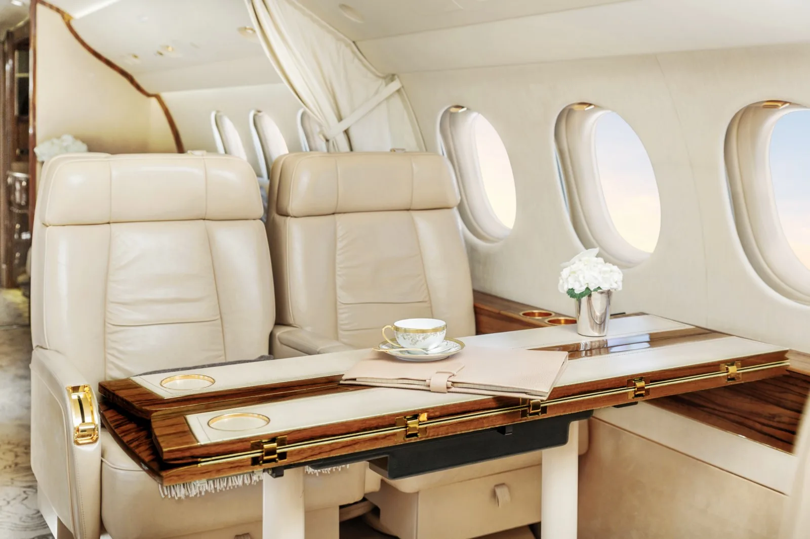 Two cream leather seats facing a fold-out wooden table set with a teacup and flowers in the aircraft cabin.