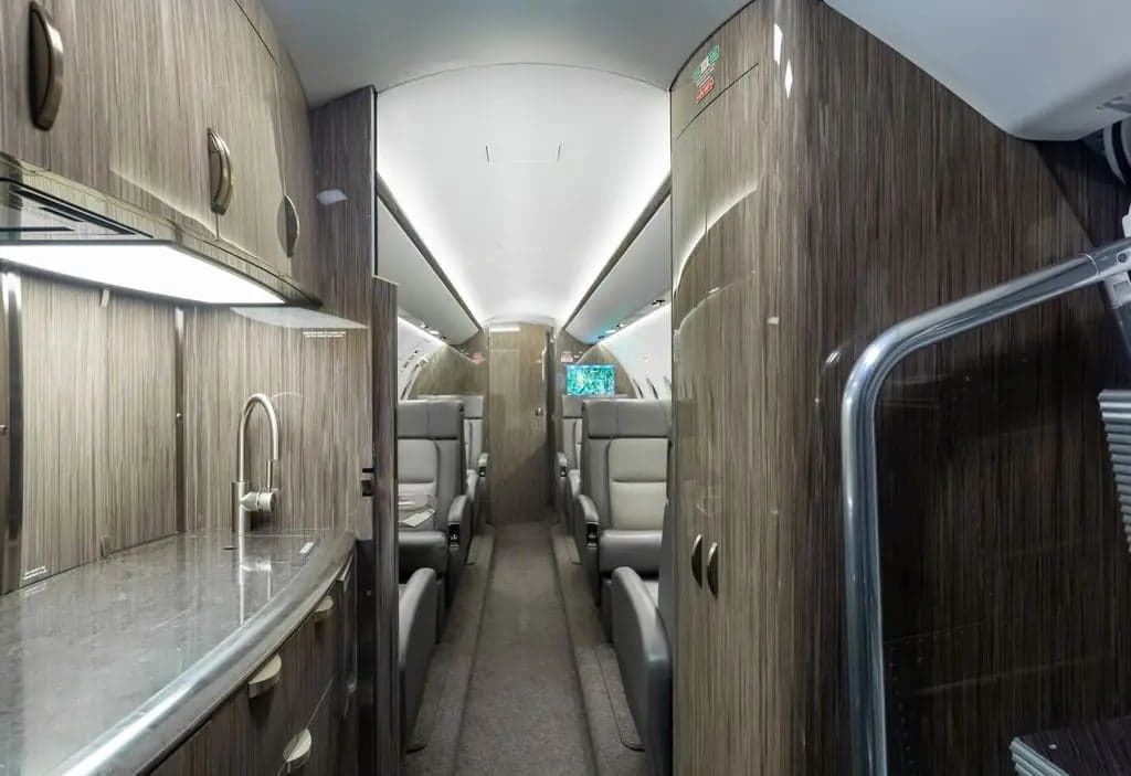 View down the aisle of the aircraft cabin, showing seats and wood-grain cabinetry.
