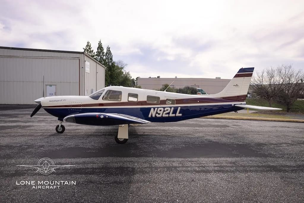 A side view of the Piper Saratoga II TC aircraft (N92LL) with blue and white paint scheme parked on an asphalt apron.