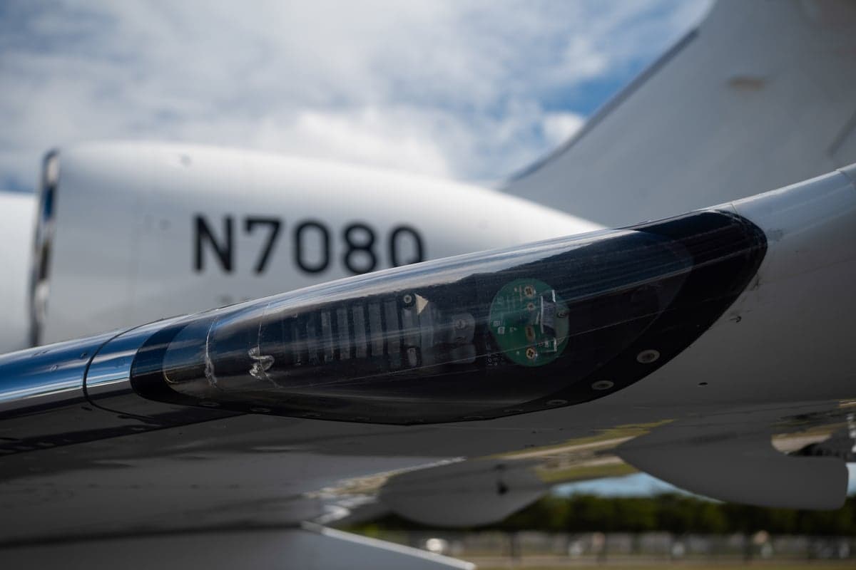 A close-up of a business jet's wing with a transparent panel revealing internal components and the tail number N708Q.