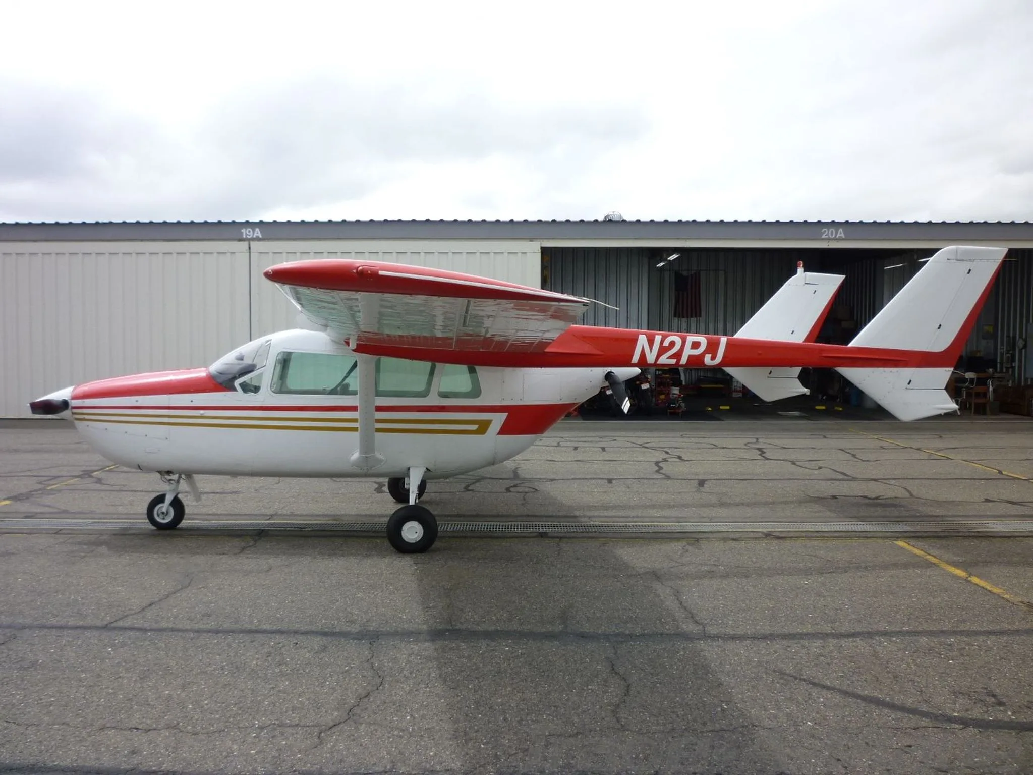 A full side profile of the white and red Cessna Skymaster N2PJ parked in front of an open hangar.