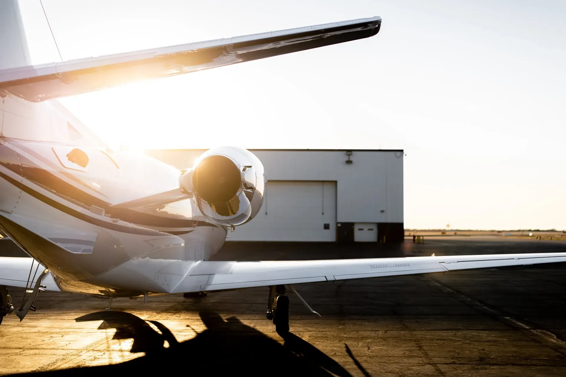A close-up of the tail and engine of a white business jet, with a hangar in the background.