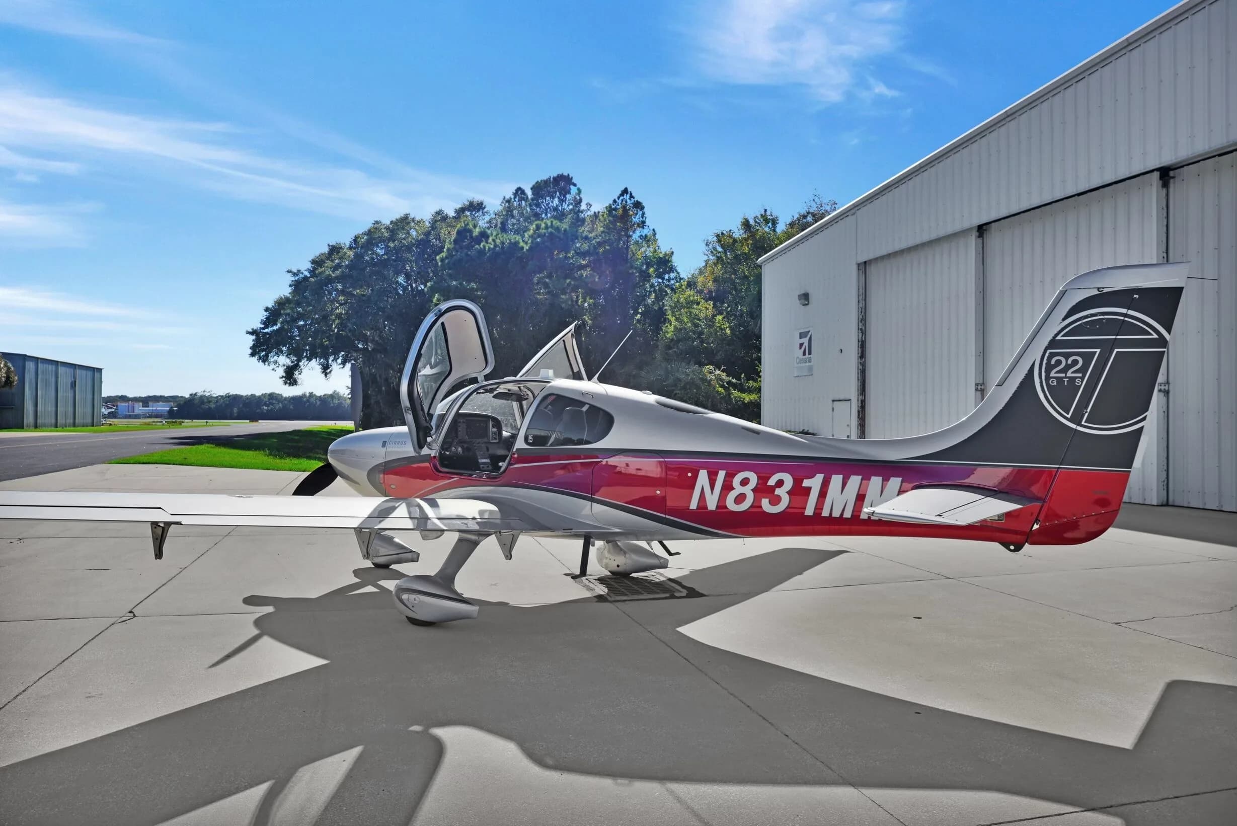 A Cirrus SR22T aircraft with red and silver paint scheme, registration N831MM, parked on an airfield with doors open.