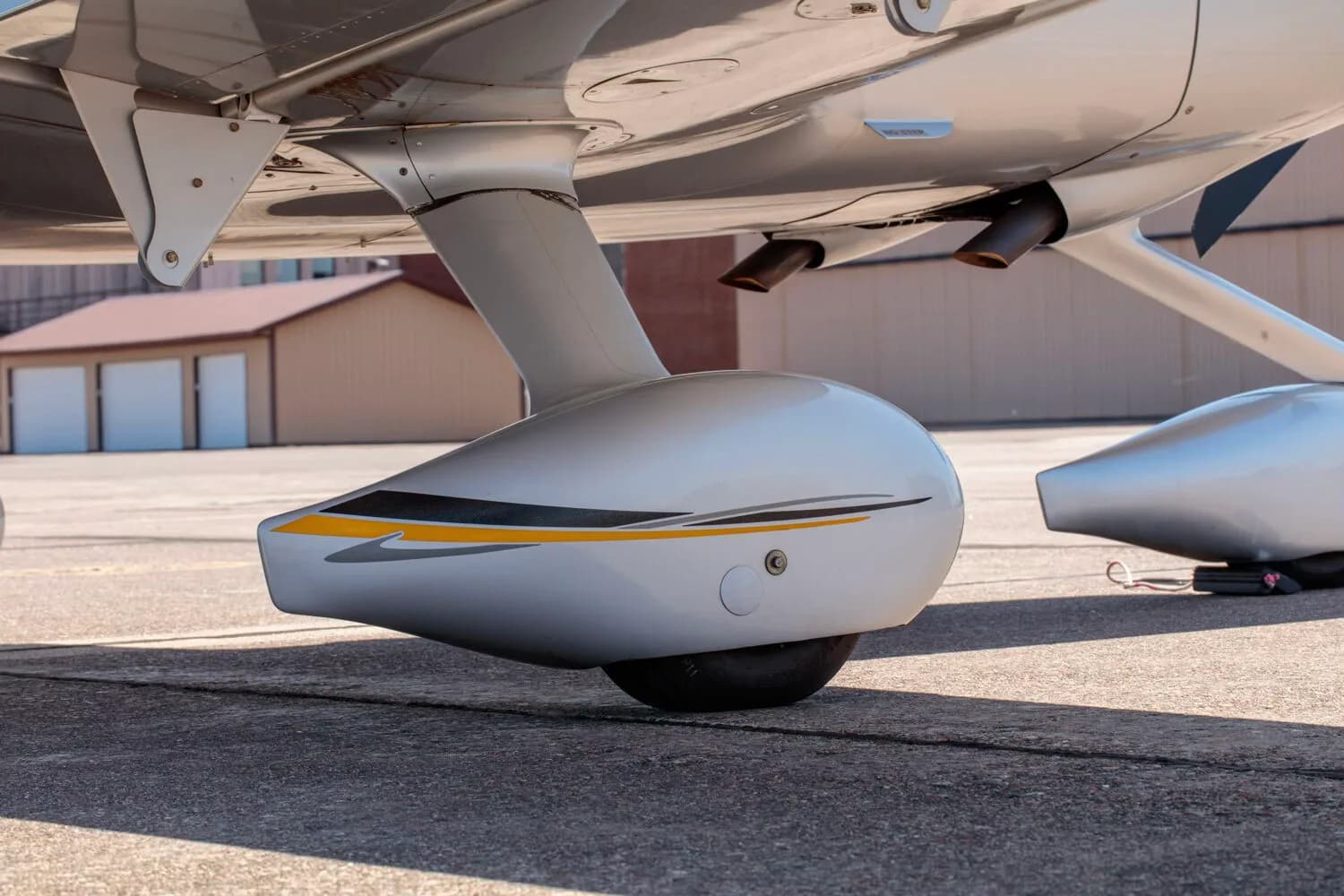 A close-up view of the main landing gear and exhaust pipes of the silver Cirrus SR22T aircraft.