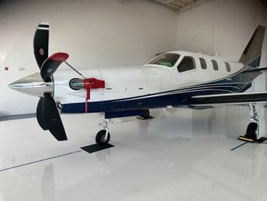 A TBM 930 aircraft is parked inside a hangar, showcasing its white and blue paint scheme.