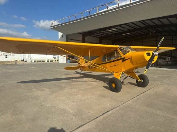 Three-quarter front view of a yellow Legend Cub aircraft with registration N267RJ, parked outside a hangar.