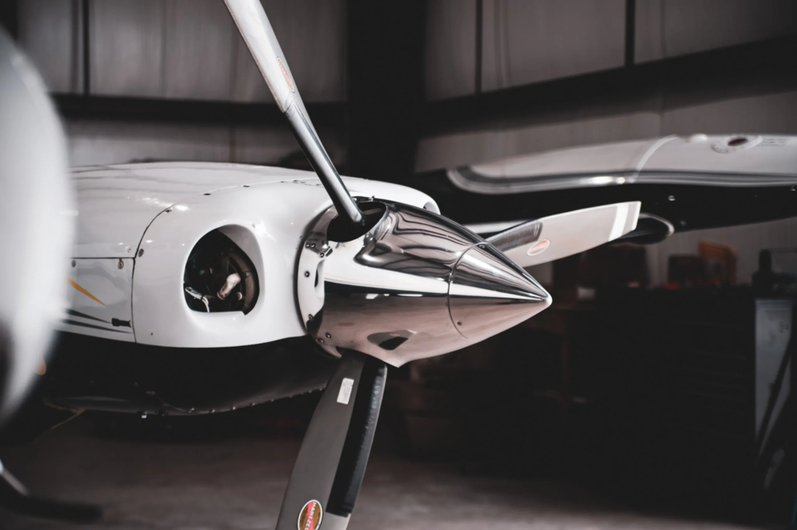 Close-up of a white aircraft's propeller and nose cone inside a hangar.