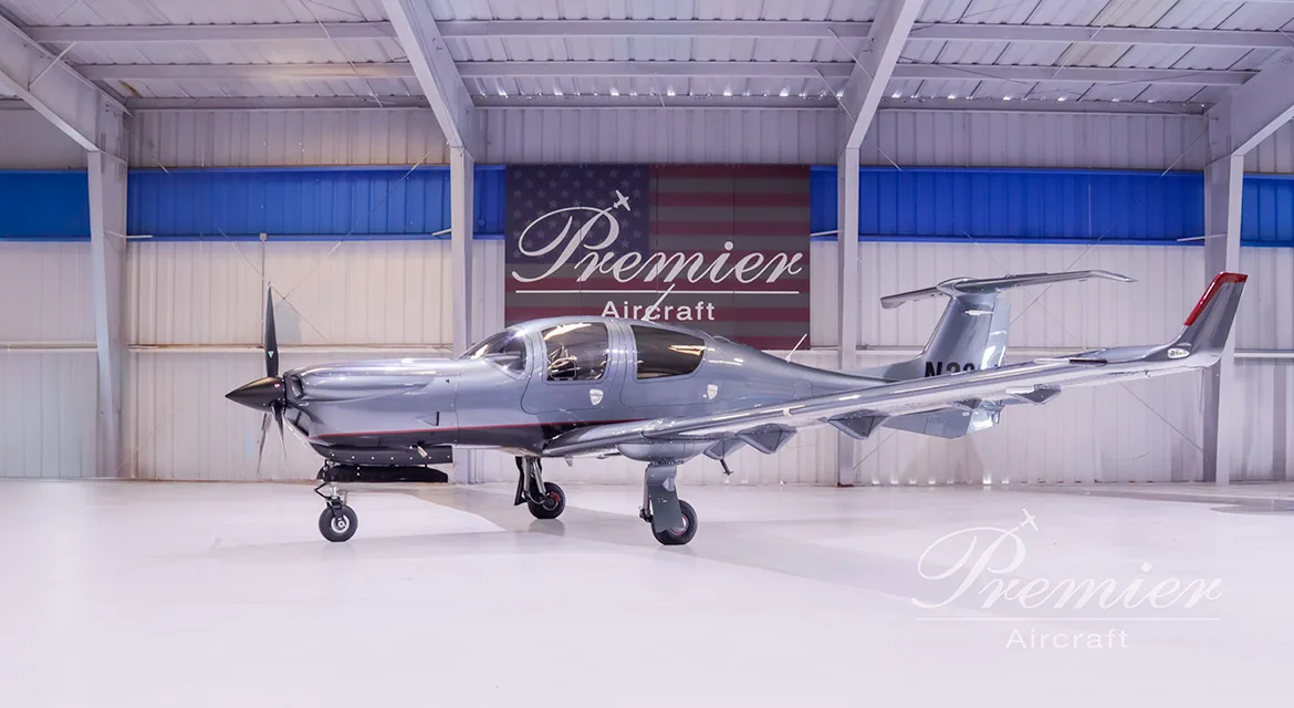 A gray Diamond DA62 aircraft is parked in a hangar with a Premier Aircraft banner in the background.