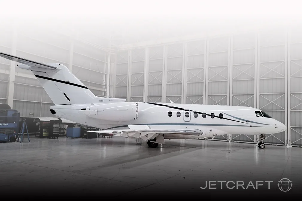 A white business jet with black and grey stripes is parked inside a large hangar.