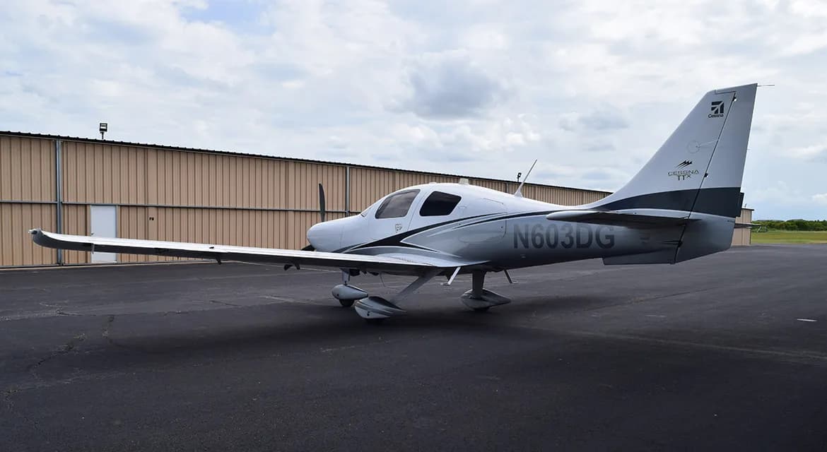 A white and grey Cessna TTx aircraft, N603DG, viewed from the rear-left on an airfield.