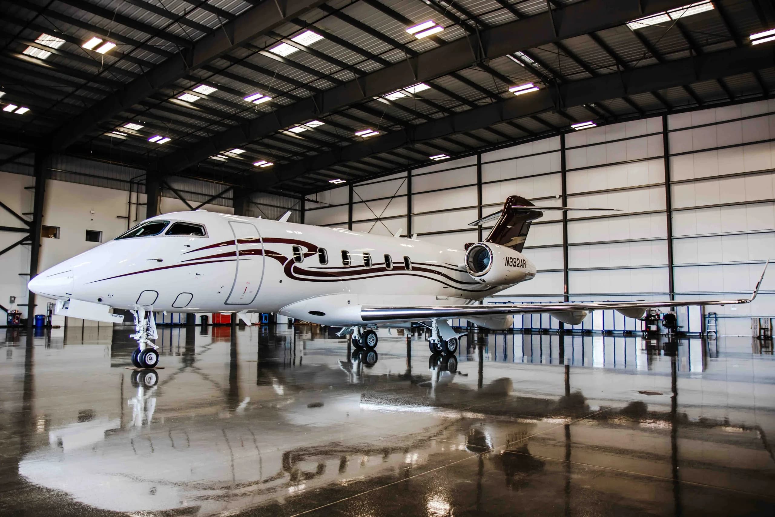 A white and brown Bombardier Challenger 300 aircraft with tail number N332AR is parked in a hangar.