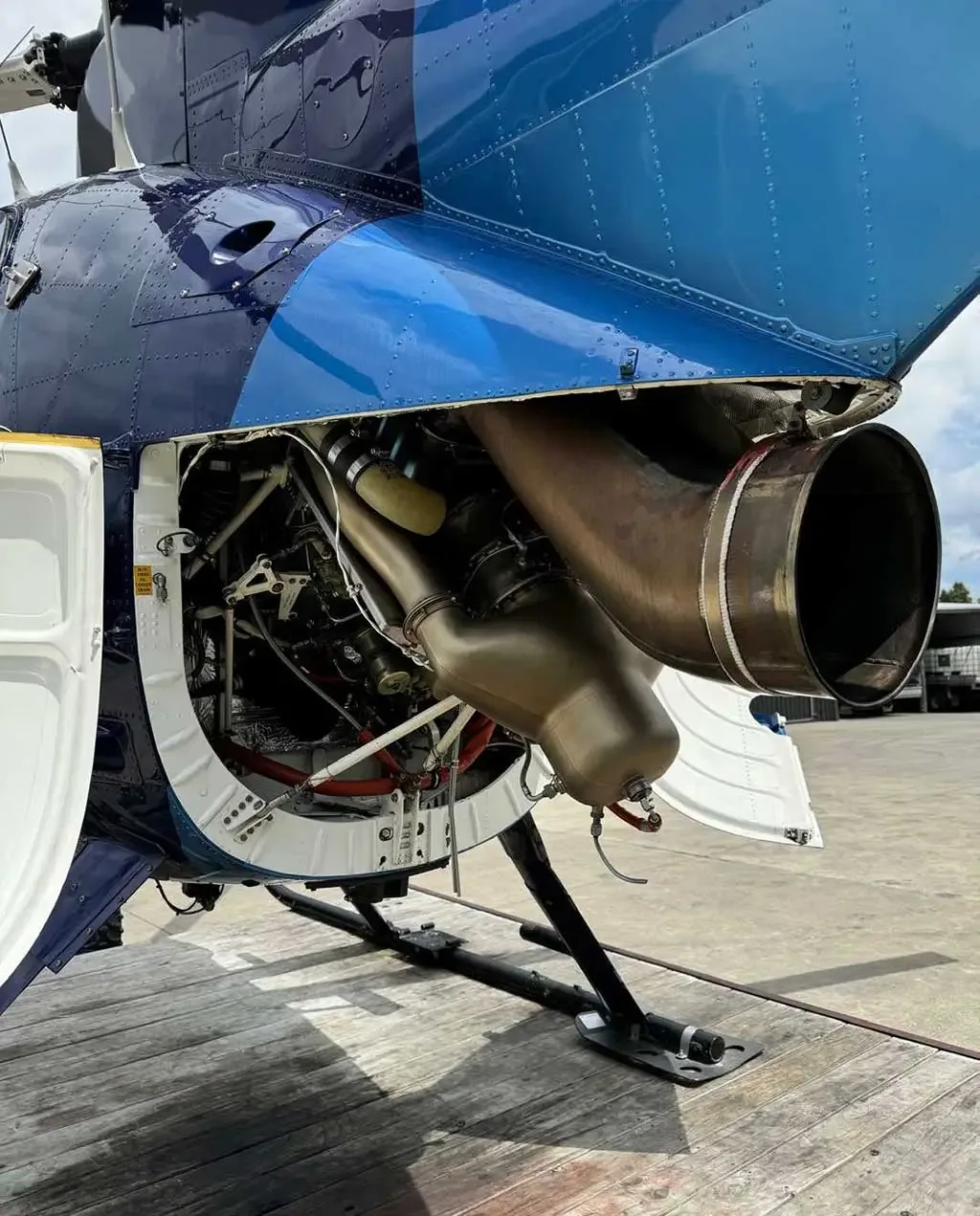 A close-up view of the open engine compartment and exhaust system of the blue and light blue MD 530 helicopter.