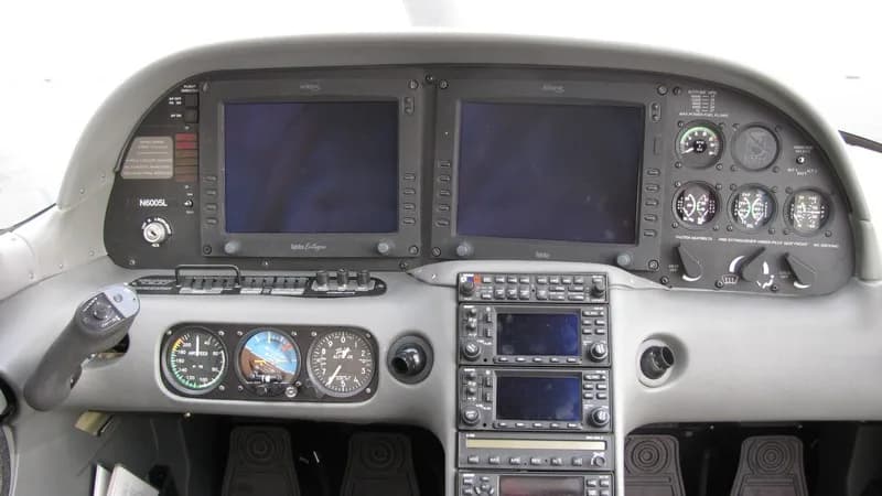 The cockpit instrument panel of a Cirrus aircraft, featuring two large display screens and traditional gauges.