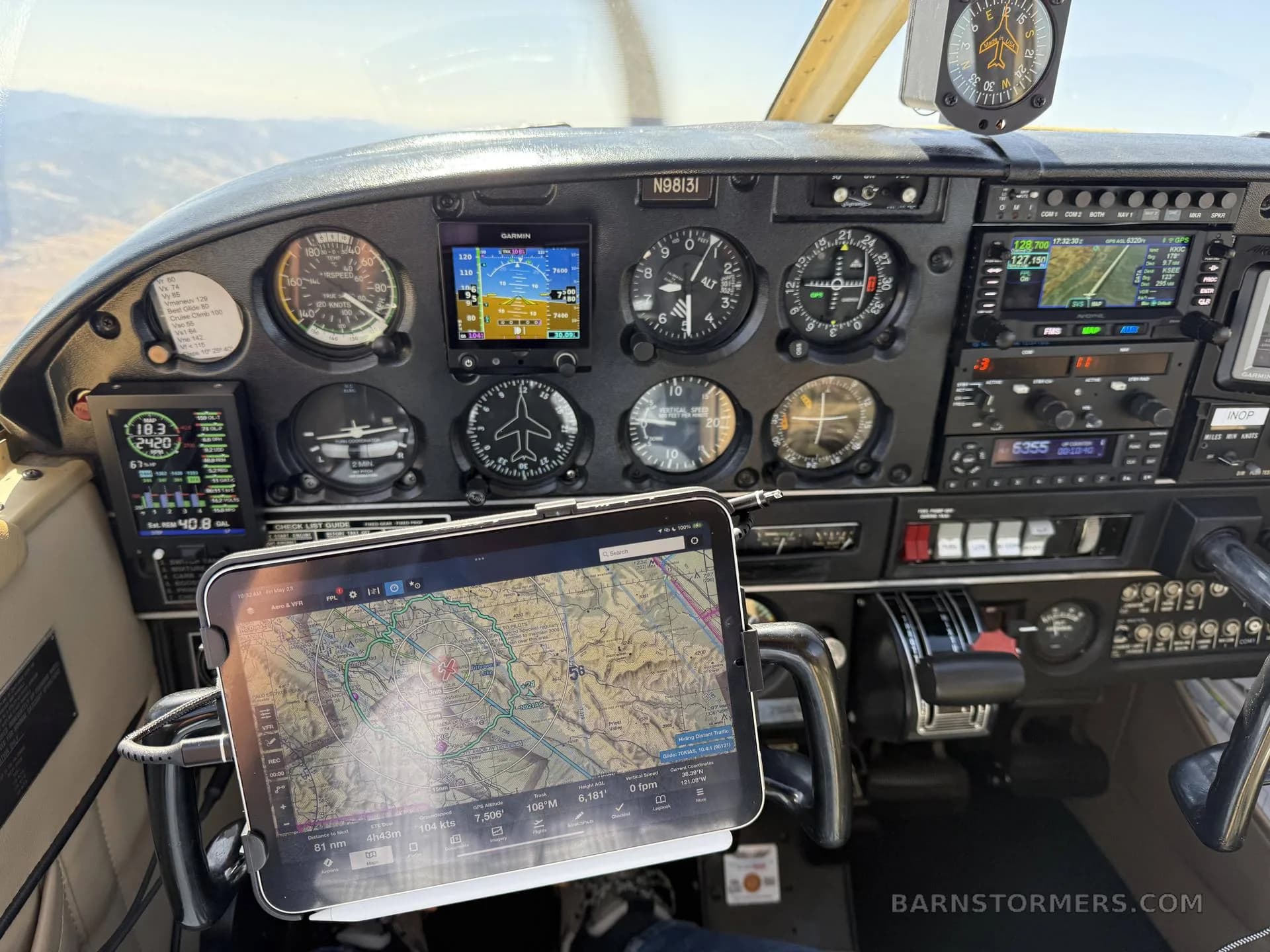 The cockpit of a light aircraft showing the instrument panel with analog gauges, digital displays, and a tablet mounted on the yoke.