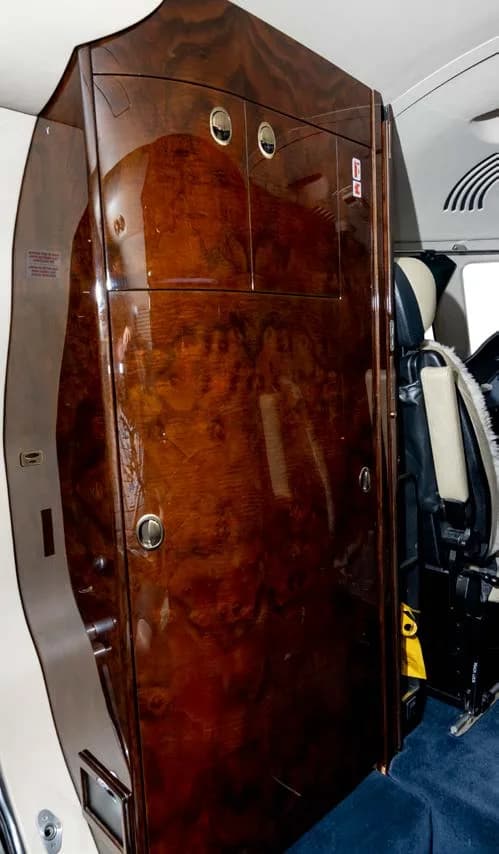 A large, highly polished dark wood cabinet with silver handles in the interior of a business jet.